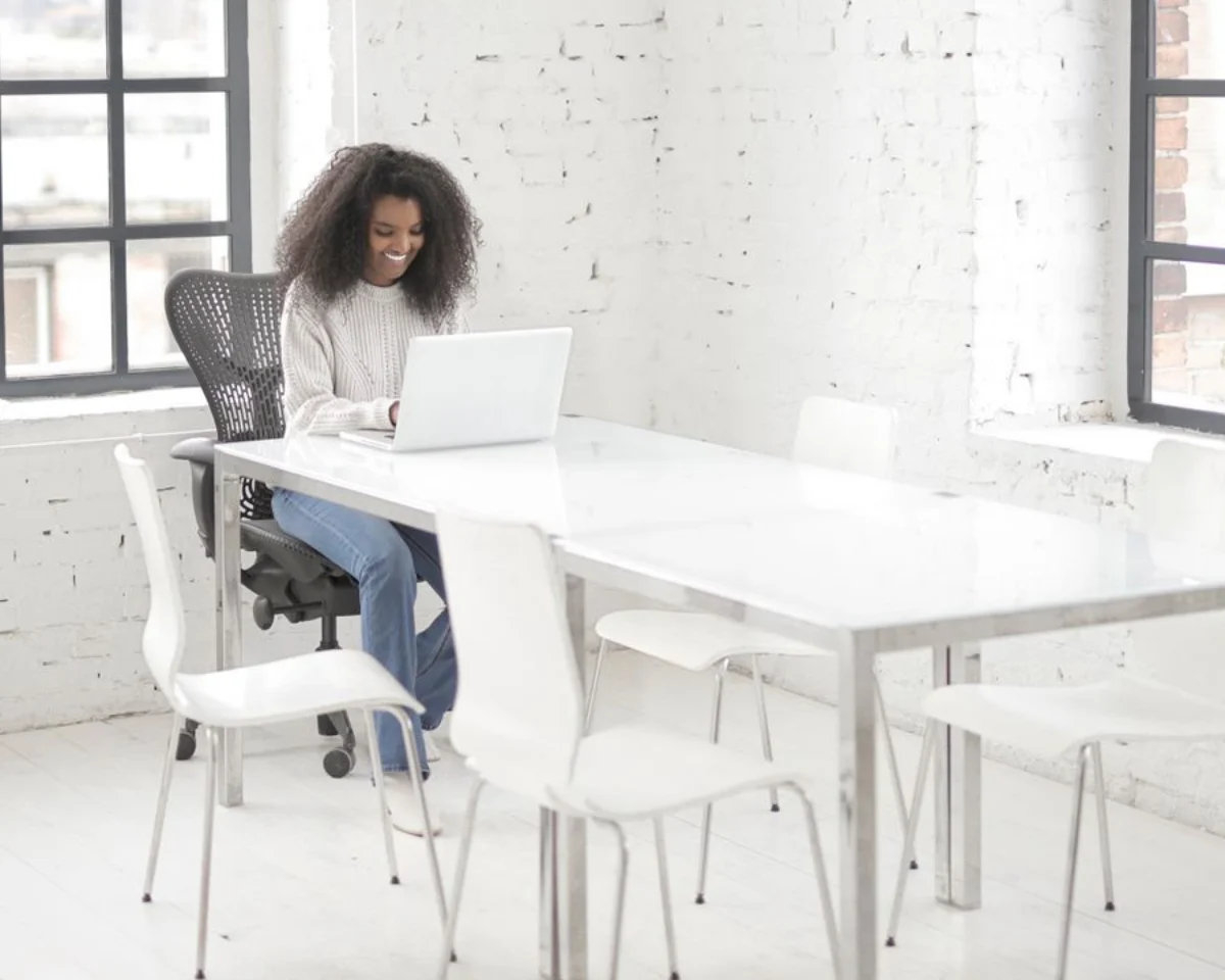 A woman working at a laptop in a bright, uncluttered workspace.